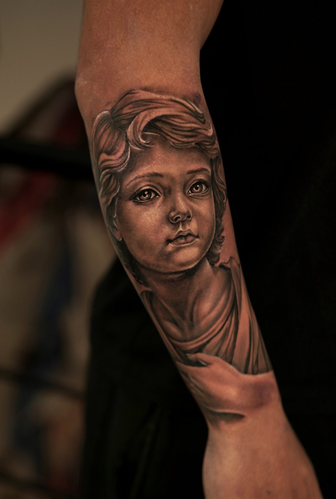 Realistic cherub statue tattoo on a forearm